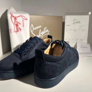  Christian Louboutin Skor - Snygga mörkblå sneakers från Christian Louboutin i mocka med klassisk röd sula och diskret broderad logga på hälen. Skorna har rund tå, platt sula och matchande mörkblå snörning. Insidan är fodrad i beige skinn för extra komfort. Perfekta för dig som gillar exklusiv streetstyle.