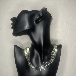 Dramatiskt vridet vintagehalsband / choker med kristaller Retro 90-talsglam - Spektakulärt halsband i silverfärgad metall med glittrande baguetteslipade kristaller. Designat för att vrida sig runt sin egen axel – skapar en spiralformad, skulptural effekt längs halsen. Tvåradigt och gnistrande i sann 90-talsglam. Ca 38–40 cm långt + förlängningskedja. Bredd ca 2,5–3 cm. Mycket gott skick – alla stenar sitter fint. Prutning ej möjlig, men jag erbjuder gärna bundlerabatt. Rensar garderob och smyckesskrin – kika gärna på mina andra annonser!  ⸻