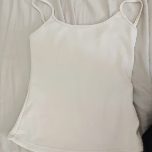 Vit enkel linnetopp med smala band - Säljer en stilren vit linnetopp med smala axelband och rak skärning. Toppen är ärmlös och har en mjuk, slät yta som känns skön mot huden. Perfekt att matcha med jeans eller kjol för en clean look. Passar storlek S och liten M. Den är lite dammig 