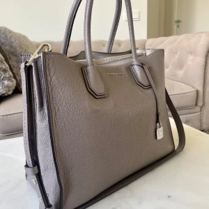 Michael Kors väska - Handväska från Michael Kors i strukturerat skinn. Väskan har två rejäla handtag, avtagbar axelrem, silverfärgade metalldetaljer och dragkedja upptill. 