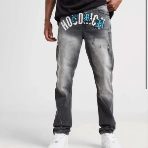 Gråa jeans med tryck från Hoodrich - Snygga grå jeans från Hoodrich med coolt tryck i vitt och blått på framsidan. Jeansen har en straight passform och slitna detaljer för en trendig look. Perfekta för dig som vill sticka ut!