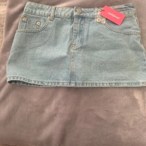 Ljusblå jeanskjol från Edithegal - Superfin ljusblå jeanskjol från Edithegal med klassisk femficksdesign, bälteshällor och knappstängning fram. Kjolen är kort och har raka linjer, perfekt till sneakers eller boots. Extra knappar medföljer. Nypris 500 köparen betalar frakten 