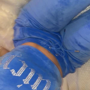 Blå Juicy Couture mjukisbyxor och topp - Blåa mjukisbyxor från Juicy Couture i mjuk velour med snörning i midjan och glittriga strasstenar på baksidan. Perfekta för en chill och trendig look. Med topp