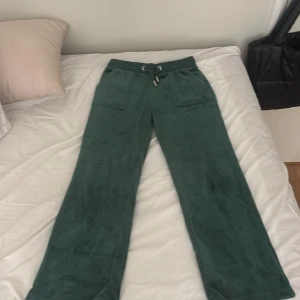 Mörkgröna mjukisbyxor Juicy Couture - Mörkgröna mjukisbyxor från Juicy Couture med bred resår i midjan och snörning. Byxorna har stora fickor fram och bak med knappdetaljer. Tillverkade i mjuk velour som känns riktigt skön mot huden. Perfekta för chill dagar eller när du vill vara extra comfy. ‼️Tröjan ligger också uppe för samma pris!!