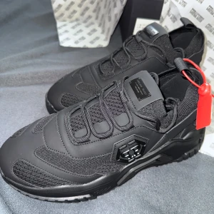 Svarta sneakers från Philipp Plein - Stilrena svarta sneakers från Philipp Plein med chunky sula och coola detaljer. Ovandelen är en mix av mesh och syntet med PP-logga på sidan och metallplatta på plösen. Skorna har snörning och sportig vibe, perfekta för dig som gillar statement-sneakers.
