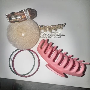 Färgglada armband och håraccessoarer - Säljer ett set med två glittriga armband i grönt och rött, ett brunt läderarmband med metallspänne, samt håraccessoarer som en rosa hårklämma, en beige hårdonut och två hårspännen med texten 'HAPPY' och 'SWEET' dekorerade med pärlor och strass.