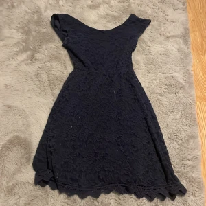 Mörkblå spetsklänning från Chi Chi London - Supersnygg mörkblå kortklänning från Chi Chi London med blommig spets och vacker v-ringning. Klänningen har korta ärmar och en feminin passform med markerad midja och volangkant nertill. Perfekt för dig som vill sticka ut med elegans.
