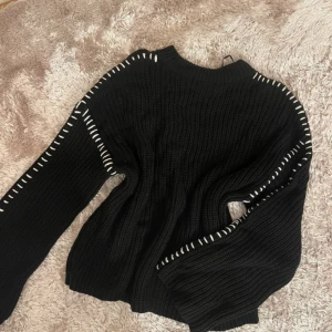 Svart stickad tröja Gina Tricot S - Svart stickad tröja från Gina Tricot i storlek S. Tröjan har vita dekorativa sömmar längs ärmar och axlar som ger en cool kontrast. Den har lång ärm och en klassisk rund halsringning. Perfekt för dig som gillar en enkel men ändå unik look.