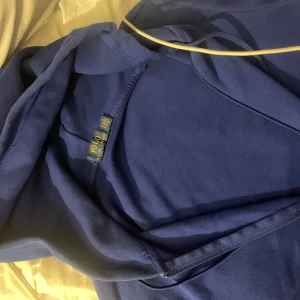 Blå hoodie från Polo Ralph Lauren - Snygg marinblå hoodie från  storlek s Polo Ralph Lauren med dragkedja och huva. Klassisk vit logga broderad på bröstet, dragsko i huvan och två fickor framtill. Perfekt för dig som gillar stilrena och bekväma plagg. Aldrig använt lite för stor så den e helt ny typ 
