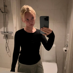 Svart långärmad basic tröja - En svart långärmad tröja med rund halsringning. Modellen är enkel och tight, perfekt att styla med jeans eller kjol. Materialet känns mjukt och stretchigt, vilket gör den skön att bära. Snygg och stilren basic som funkar till allt.