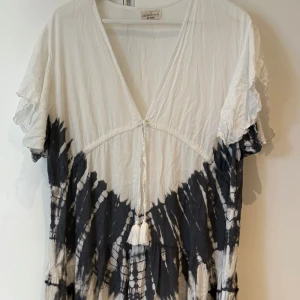 Bohemisk tie-dye klänning Odd Molly - Superskön kortklänning från Odd Molly i svart och vitt tie-dye-mönster. Klänningen har v-ringning, snörning med tofsar framtill och korta volangärmar. Lätt och luftig i bomull, perfekt för en avslappnad och cool stil.