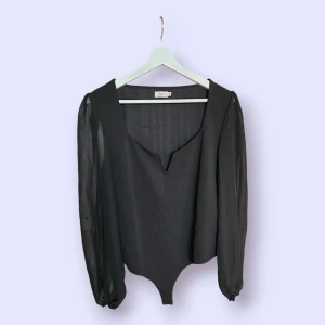 Svart body i storlek XXL (passar andra storlekar) från Nelly - Svart body med långa, genomskinliga ärmar och en v-ringad halslinje. Den har en figurnära passform. Storleken är i XXL men jag upplever att den passar L - XL. Aldrig använd.