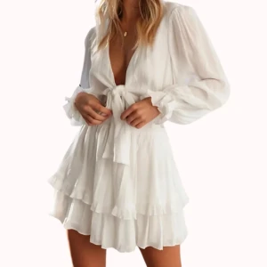 Vit omlottklänning med volanger - Superfin vit kortklänning med omlott och knyt framtill. Klänningen har långa ärmar, v-ringning och flera lager volanger i kjolen för en flowy känsla. Perfekt för sommarens alla tillfällen och ger en fräsch och luftig look.