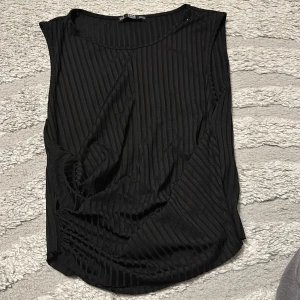 Svart ribbad ärmlös topp Zara - Svart ärmlös topp från Zara med ribbat tyg och rund halsringning. Snyggt randigt mönster i materialet ger en cool look. Perfekt att styla med jeans eller kjol för en trendig outfit.