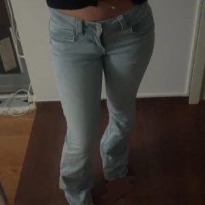 Ljusblå bootcut jeans med fickdetalj - Säljer ett par ljusblå jeans med bootcut-modell och snygga fickdetaljer bak med knapp. Jeansen har klassisk femficksdesign, låg midja och är tillverkade i mjukt denimtyg. Perfekta för dig som gillar en avslappnad men trendig look.