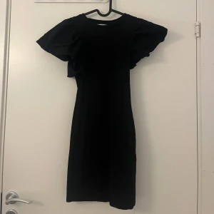 Svart kort klänning med puffärmar Zara - Supersnygg svart kort klänning från Zara med puffiga korta ärmar och rund halsringning. Klänningen har en tight passform och är gjord i ett stretchigt material som sitter perfekt. Perfekt för dig som vill sticka ut med coola detaljer!