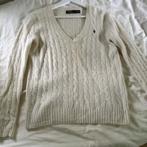 Kabelstickad vit tröja Polo Ralph Lauren - Kabelstickad vit tröja från Polo Ralph Lauren med v ringning. Fin hösttröja. Köpt på zalando för 2300. Finns qrkod så man kan kolla att den är äkta. Storlek m och sitter åt det tajta hållet. Ganska tunt material. Den är använd så är lite nopprig men inte mycket och inga mer tecken på användning. Den är vitbeige.