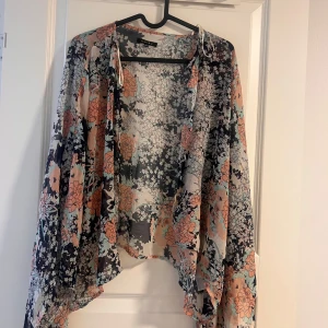 Blommig blus från Amisu XS/S - Säljer en luftig blommig blus från Amisu i storlek XS/S. Blusen har vida ärmar och ett vackert mönster i persikoorange, svart, beige och mintgrönt. Perfekt för dig som gillar boho-vibbar och lätta material.