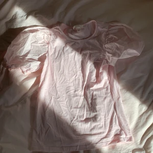 Ljusrosa puffärm blus från H&M XS - Supersöt ljusrosa blus från H&M i bomull med korta puffärmar och rund halsringning. Perfekt för dig som gillar en romantisk och trendig look. Enkel att matcha med både jeans och kjol.