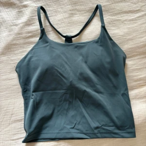 Mörkgrön linnetopp från Relode - Supersnygg mörkgrön linnetopp från Relode med tunna axelband och racerback. Topp i mjukt och stretchigt syntetmaterial som sitter skönt på kroppen. Enkel och stilren design med Relode-logga på ryggen.