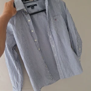 Randig skjorta från GANT i bomull - Snygg blåvit randig skjorta från GANT med klassisk krage och bröstficka med broderad logga. Skjortan har långa ärmar och knäppning framtill. Perfekt för en clean och stilren look.