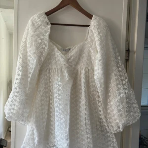 Student klänning NA-KD - Superfin vit kortklänning från NA-KD med broderade blommor och puffiga långärmar. Klänningen har v-ringning och är tillverkad i ett lätt, transparent material med fodrad insida. Perfekt för sommarens alla tillfällen!