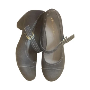 Mary Janes - Gråbruna Mary Janes i storlek 37. Bekväma med låg klack och spänne. Skorna är använda och har slitage på remmarna och bakre delen, se bilder.