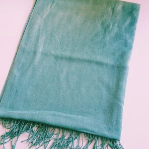 Turkos halsduk med fransar - En stilren turkos halsduk med tunna fransar i ändarna. Halsduken är lång och mjuk, perfekt att svepa runt halsen för extra värme. Enkel design utan mönster, vilket gör den lätt att matcha med olika outfits.  Helt skick dock noppror