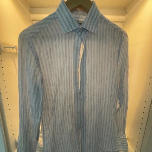 Randig linneskjorta från Dressmann - Snygg vit skjorta med ljusblå ränder från Dressmann. Slim fit-modell i premium linne som ger en luftig och fräsch känsla. Klassisk krage, knäppning framtill och långa ärmar. Perfekt för dig som gillar stilrena och fräscha plagg.