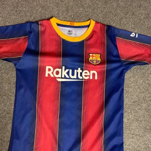 FC Barcelona Messi 10 matchtröja - Säljer en ikonisk FC Barcelona fotbollströja med Messi 10 på ryggen. Tröjan har klassiska blå och röda vertikala ränder, gul krage och klubbmärke på bröstet. Tillverkad i lätt och ventilerande material, perfekt för dig som älskar fotboll och vill bära din idol.