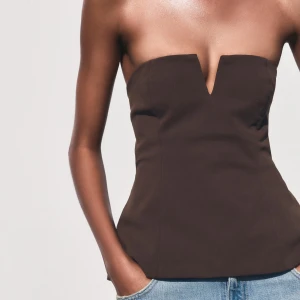 Brun axelbandslös tubtopp med V-ringning - Snygg brun tubtopp med markerad V-ringning framtill. Axelbandslös design som sitter tight över bysten och har en lätt utsvängd passform nedtill. Perfekt att styla med jeans eller kjol för en trendig look.