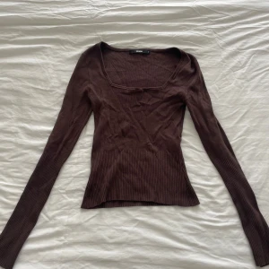 Brun ribbad tröja Bik Bok - Mörkbrun tröja från Bik Bok med lång ärm och fyrkantig ringning. Tröjan har ribbade detaljer vid midjan och ärmarna, vilket ger en snygg och figurnära passform. 