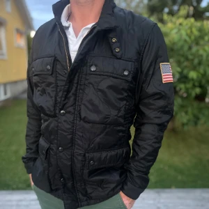 Feild jacka från ralph lauren - Svart feild jacka från Denim & Supply Ralph Lauren med amerikansk flagga på ärmen. Jackan har fyra fickor framtill med knappar, hög krage och stängs med både dragkedja och tryckknappar. Perfekt för dig som gillar stilren och sportig look.