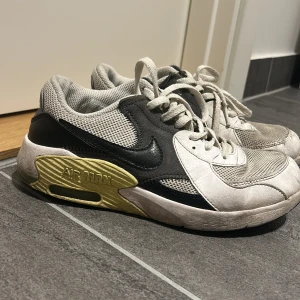 Nike Air Max sneakers vit/svart/gul - Nike Air Max sneakers i vitt, svart och gult med mesh och skinnpaneler. Klassisk Air Max-dämpning, snörning och rund tå. Snygg kontrast mellan de svarta detaljerna och den gula sulan. Perfekta för dig som gillar retrovibbar och streetstyle.