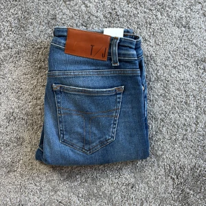 Blå jeans från Tiger of Sweden - Snygga blå jeans från Tiger of Sweden med klassisk femficksdesign och bruna sömmar. Jeansen har en normal passform och är tillverkade i mjukt bomullsjeansmaterial. Perfekta för dig som gillar stilrena och tidlösa jeans.