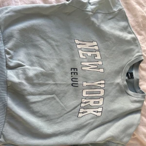 Ljusblå sweatshirt - En fin ljusblå sweatshirt med trycket 'NEW YORK EE.UU' framtill. Tröjan har rund halsringning, kommer inte mer till användning. Kan ha lite fläckar som inte går bort men syns knappt. Kontakta gärna innan köp!