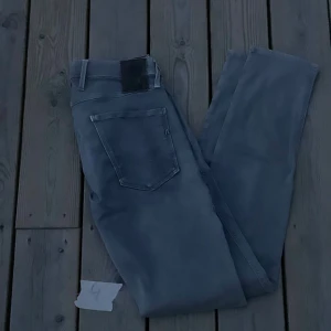 Grå Replay Anbass slim fit jeans 29-32 - Snygga grå jeans från Replay, modell Anbass. Klassisk femficksdesign med Replay-logga på fickan och svarta detaljer. Jeansen har en smal passform och är tillverkade i mjukt bomullsmaterial med stretch för extra komfort.