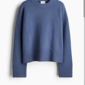 Blå stickad oversized tröja - Säljer en blå stickad tröja med oversized passform och breda ribbade muddar vid ärmslut och nederkant. Tröjan har rund halsringning och långa ärmar, perfekt för en chill och avslappnad stil.