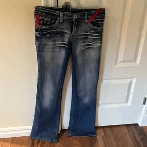 Blå bootcut jeans - Snygga blå bootcut jeans med röda detaljer vid fickorna. Baksidan har broderade blommor och snygg detalj på bakfickorna. Jeansen är knappt använda och inte alls slitna längst ner (se bild). 