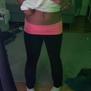 Victoria secret PINK rosa fold over midja - Svarta mjukisbyxor från PINK med bred, låg rosa midja dekorerad med små glittriga detaljer och tryckt logga bak. Byxorna har en tight passform upptill och lätt utsvängda ben. Perfekta för chill eller träning.