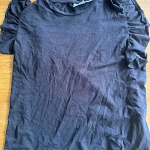 Svart t-shirt med puffärm Gina Tricot - Svart t-shirt från Gina Tricot med korta puffärmar som ger en trendig vibe. Tillverkad i mjuk bomull och har en klassisk rund halsringning. Perfekt för dig som gillar en enkel men ändå snygg look.