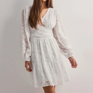 Vit klänning från Neo Noir - Superfin vit kortklänning från Neo Noir med v-ringning, långa puffärmar och knappar framtill. Klänningen är köpt på Nelly och är använd en gång. Nypris:899