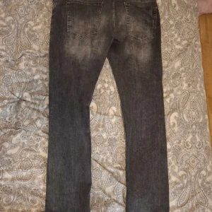 Grå slitna jeans med hål - Säljer ett par grå jeans med slitningar och hål på benen för en riktigt edgy look. Jeansen har fem fickor, normal passform och är tillverkade i klassiskt denimtyg.