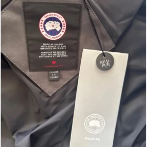 Canada Goose svart dunjacka med päls - Säljer en svart Canada Goose dunjacka i storlek S med äkta päls på huvan. Jackan har en klassisk pufferstil, stor huva och tydlig logga på ärmen. Perfekt för kalla vinterdagar och riktigt snygg streetstil.