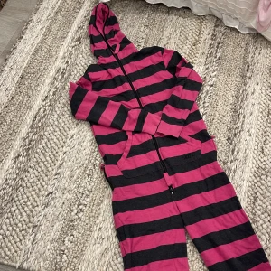 Randig rosa och svart onepiece - En onepiece med breda rosa och svarta ränder, huva och hel dragkedja framtill. Perfekt för att mysa runt hemma. 