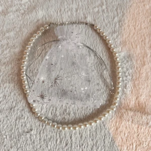 Klassiskt pärlhalsband i vitt - Ett stilrent halsband med vita pärlor i rund form, perfekt för dig som gillar en tidlös och elegant look. Levereras i en söt organzapåse med silverdetaljer och stjärnmönster. Halsbandet har en enkel och klassisk design som passar till många olika stilar. Priset är ej hugget i sten 