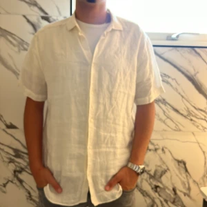 Vit linneskjorta från Riley - Snygg vit skjorta från Riley i 100% linne. Skjortan har korta ärmar, klassisk krage och knäppning framtill. Perfekt för varma dagar med sin luftiga och stilrena design. Regular fit och passar dig som gillar en clean och fräsch look.