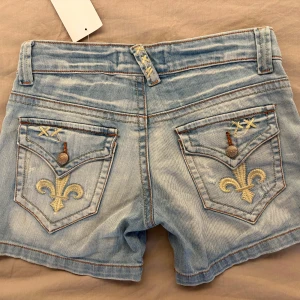 Ljusblå lågmidjade jeansshorts  - Snygga lågmidjade ljusblå jeansshorts med broderade detaljer och dekorativa sömmar. Shortsen har klassisk femficksmodell, låg midja och coola broderier på bakfickorna 