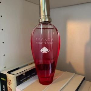Escada Sorbetto Rosso parfym - Fräsch parfym från Escada, Sorbetto Rosso, i en snygg röd-rosa glasflaska med silverfärgad kork. Flaskan har en elegant, avlång form och en vattenmelon-symbol på framsidan. Perfekt för dig som gillar fruktiga och somriga dofter. 100ml helt ny