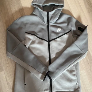 Grå Nike tech - Snygg grå tech från Nike med svart dragkedja och huva. Tröjan har en sportig look med svarta detaljer och logga på bröstet. Perfekt för dig som gillar streetwear och vill ha något bekvämt och stilrent. Hör av er vid intresse, kan gå ner vid snabb affär💯💯